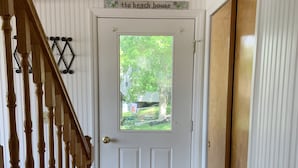 A white door with a window, a wooden staircase, and a sign above the door that reads "the beach house". - ‘Not To Worry’ Waterfront Home (Wolcott)