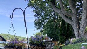 A garden with hanging flower baskets, a wooden bench, and a stone wall. - ‘Not To Worry’ Waterfront Home (Wolcott)
