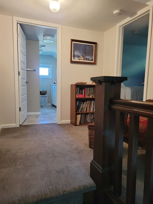 Un couloir doté d’un sol recouvert de moquette, d’une bibliothèque en bois, d’un tableau encadré accroché au mur et d’une porte donnant sur une autre pièce.