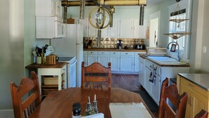 Une cuisine avec des meubles blancs, une table à manger en bois et un luminaire suspendu.