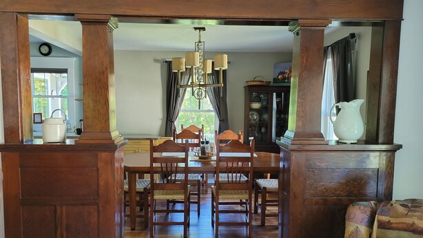 Un coin repas avec une table et des chaises en bois, un lustre et un buffet sur lequel est posée une carafe.