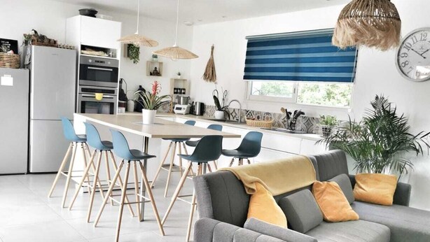A modern kitchen with white cabinets, a built-in oven, and a dining area with a grey sofa and blue chairs. - Villa swimming pool barbecue terrace in the heart of Provence (Neoules)