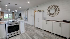 A modern kitchen with white cabinetry, a stainless steel oven, pendant lights, and a decorative mirror on the wall.