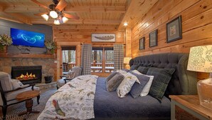 Una camera da letto accogliente in legno con camino, un letto comodo, televisione e un balcone con vista sulla foresta circostante.