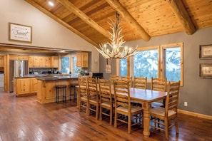 Une cuisine spacieuse avec des meubles en bois et un grand îlot central, un coin repas avec une table et des chaises en bois, et un plafond avec des poutres apparentes.
