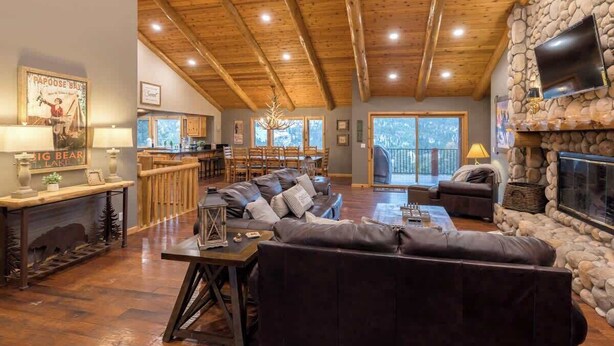 Un vaste espace de vie agrémenté d’une cheminée en pierre, de poutres apparentes en bois et d’un grand canapé.