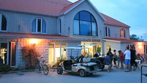 A building with a red roof and large windows, a golf cart parked in front, and people standing outside. - Great Blue Resorts - Golden Beach Resort (Alnwick/Haldimand)