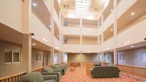 Een hotel lobby met een hoge plafond, meerdere verdiepingen en een centraal zithoek met banken en een vloerkleed.