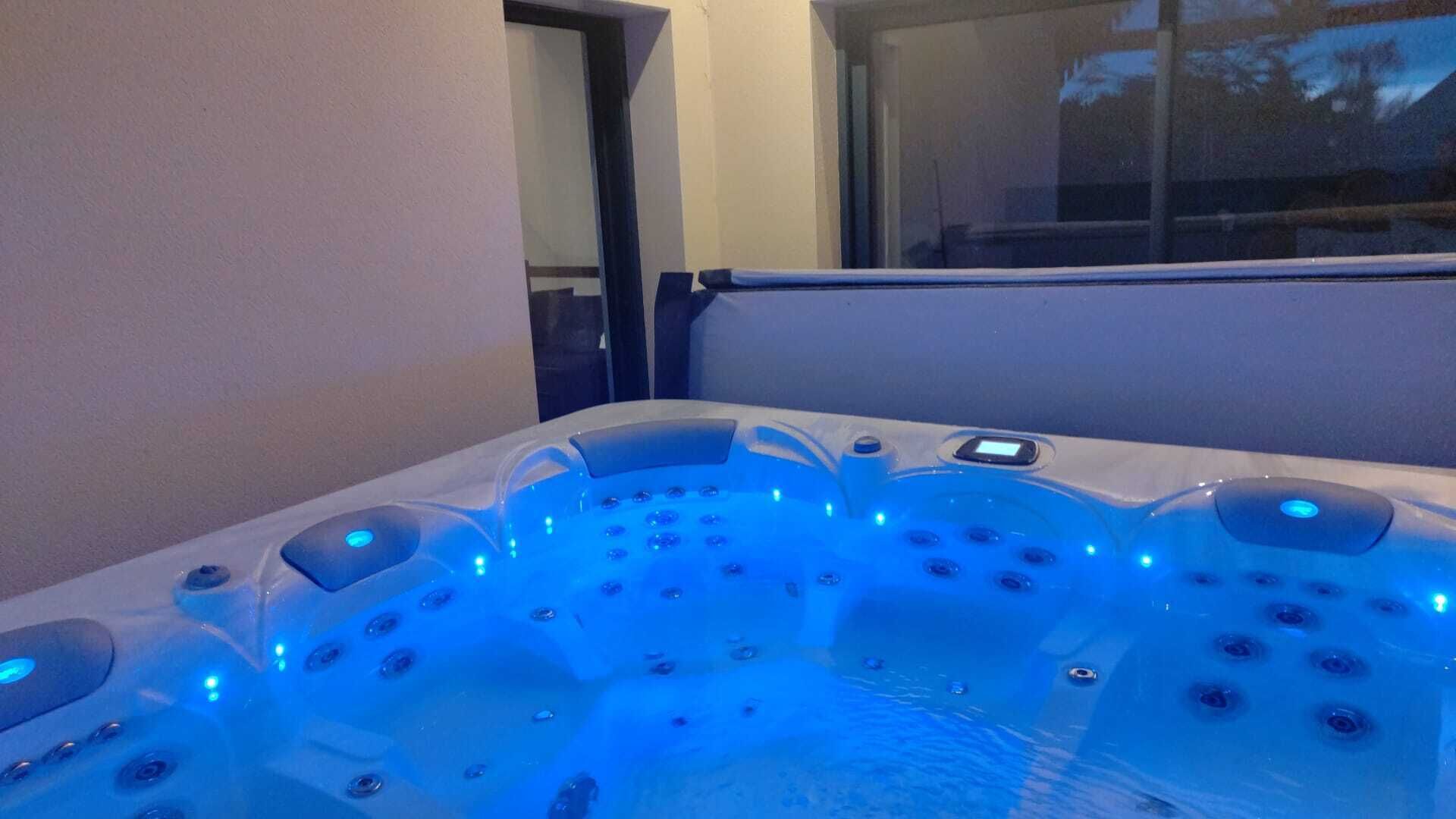 Ein Whirlpool mit mehreren Düsen, beleuchtet von blauem Licht, in einem Raum mit Fenster und Tür.