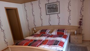 A bedroom with a wooden bed, a nightstand, a bedside table, a framed picture on the wall, and a door. - Ferienwohnung Tremmbach (Lemberg/Salzwoog)