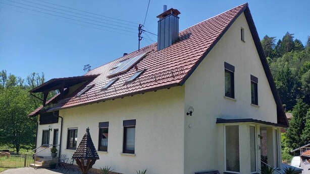 A two-story house with a red-tiled roof, a chimney, and a small porch with a bench. - Ferienwohnung Tremmbach (Lemberg/Salzwoog)