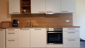 A modern kitchen with white cabinetry, a stainless steel oven, and a wooden countertop. - Ferienwohnung Tremmbach (Lemberg/Salzwoog)
