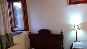 A bedroom with a bed, a window with curtains, a bedside lamp, and a framed picture on the wall. - Boarding house for students and young professionals (București)