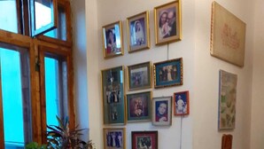 A dining area with a round table set for four, surrounded by chairs. The table is covered with a white tablecloth and has plates, cutlery, and glasses arranged for a meal. There are potted plants on the windowsill, and the wall is decorated with framed photographs. - Boarding house for students and young professionals (București)