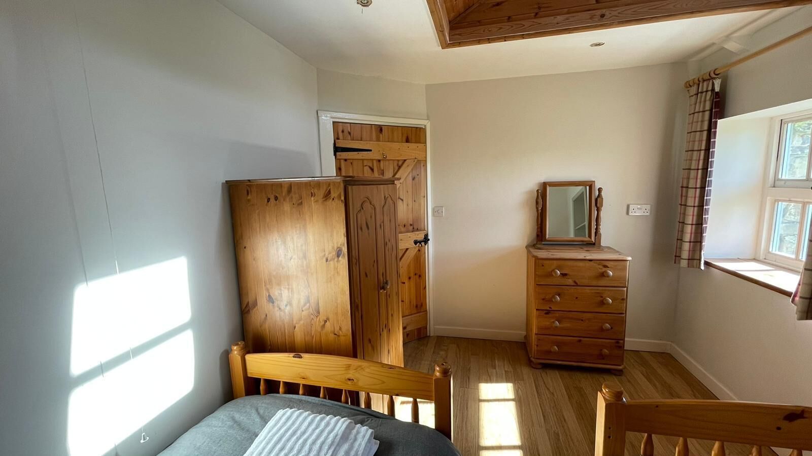 A bedroom with a wooden bed, a dresser, and a window with curtains.