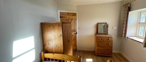 Une chambre à coucher avec un lit en bois, une commode et une fenêtre avec des rideaux.