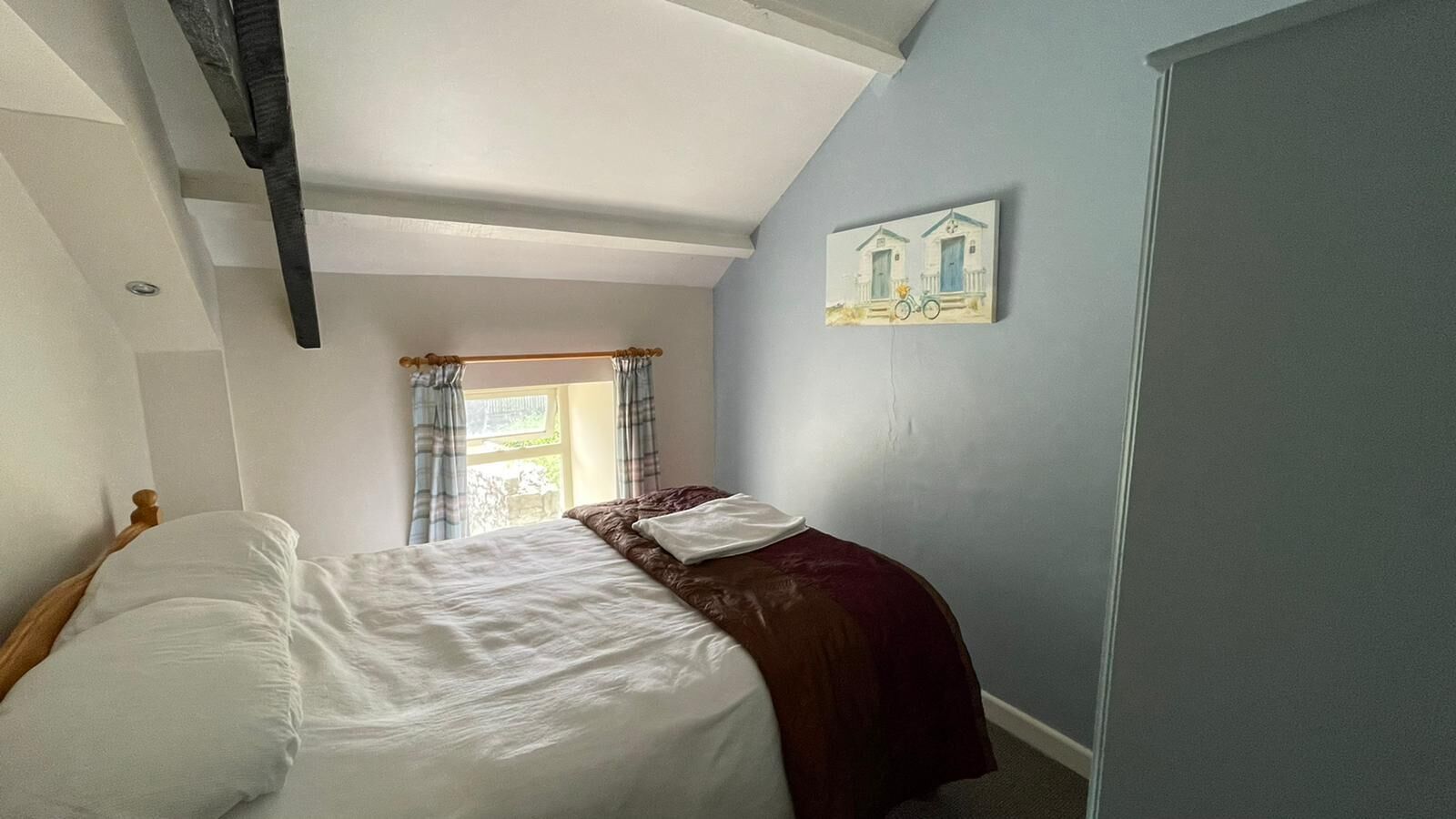 Un dormitorio con cama, ventana con cortinas, un cuadro en la pared y una puerta.