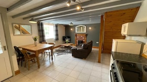 Un salon chaleureux avec une cheminée, un coin repas avec une table et des chaises en bois, et une cuisine équipée d’une cuisinière et d’un four à micro-ondes.