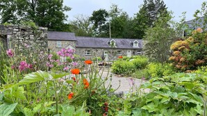 Un bâtiment en pierre avec un jardin devant, comprenant différentes plantes et fleurs.