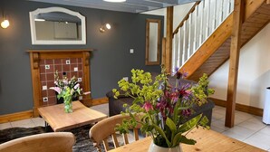Un coin repas avec une table et des chaises en bois, un vase avec des fleurs, une cheminée et un escalier.