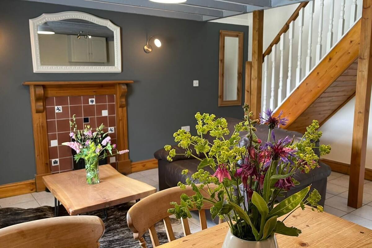 A dining area with a wooden table and chairs, a vase with flowers, a fireplace, and a staircase.