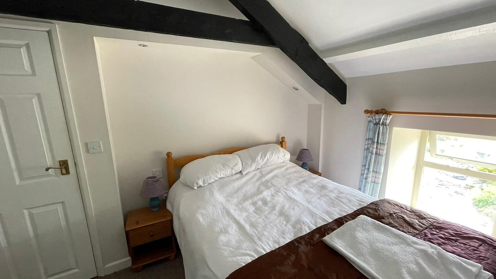 Une chambre à coucher avec un lit, une table de chevet, une lampe et une fenêtre avec des rideaux.