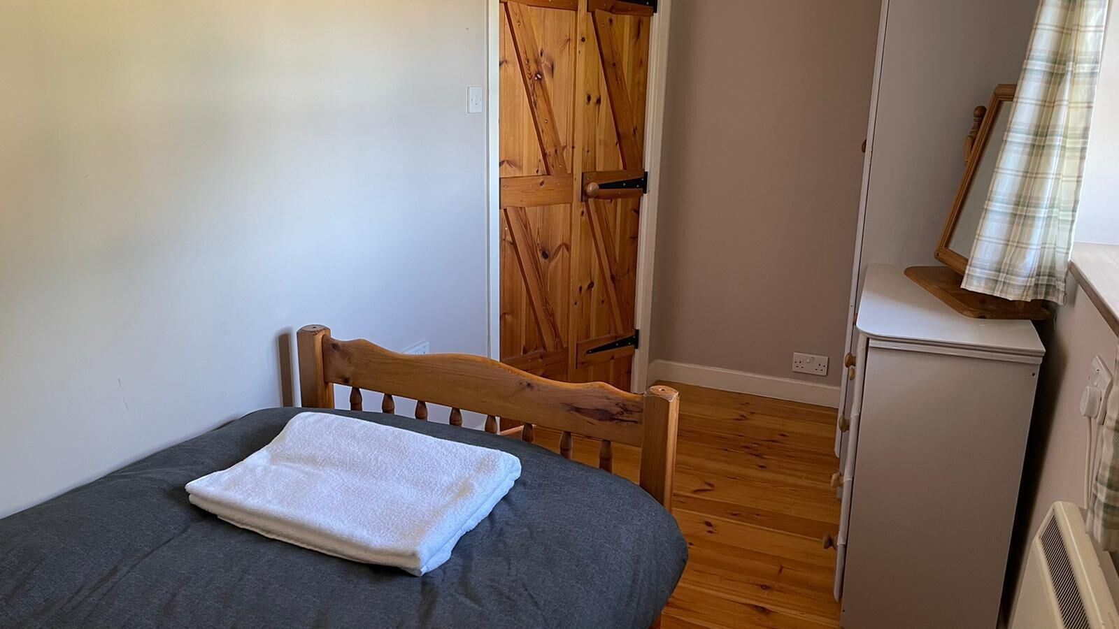 A small bedroom with a single bed, a wooden door, a small heater, and a mirror on the wall.