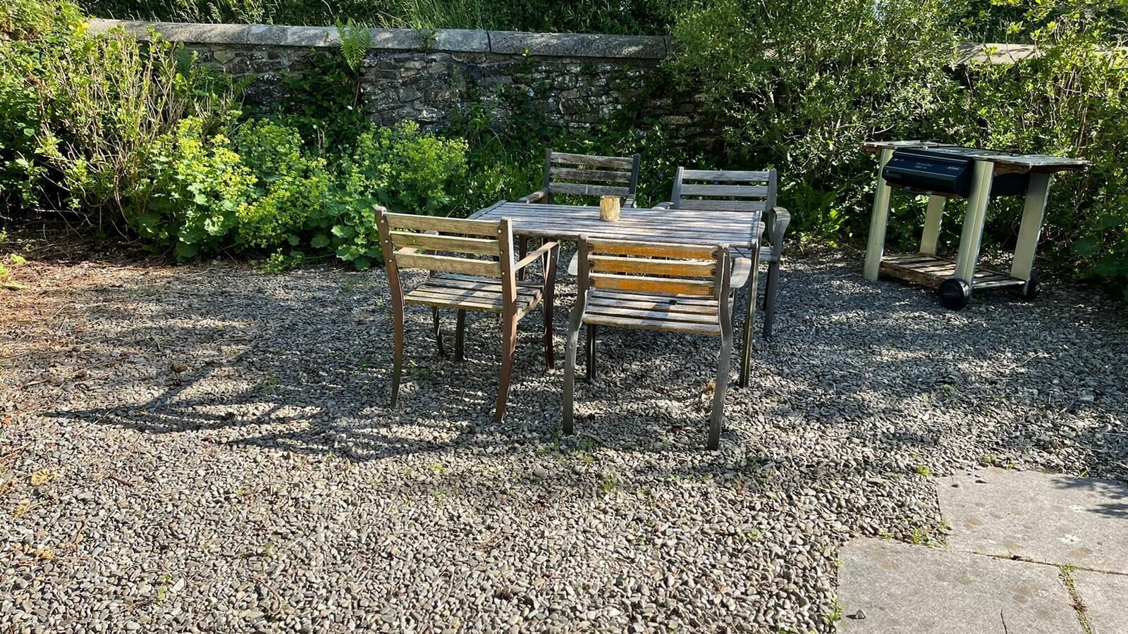 An outdoor seating area with a stone wall, gravel ground, and greenery.