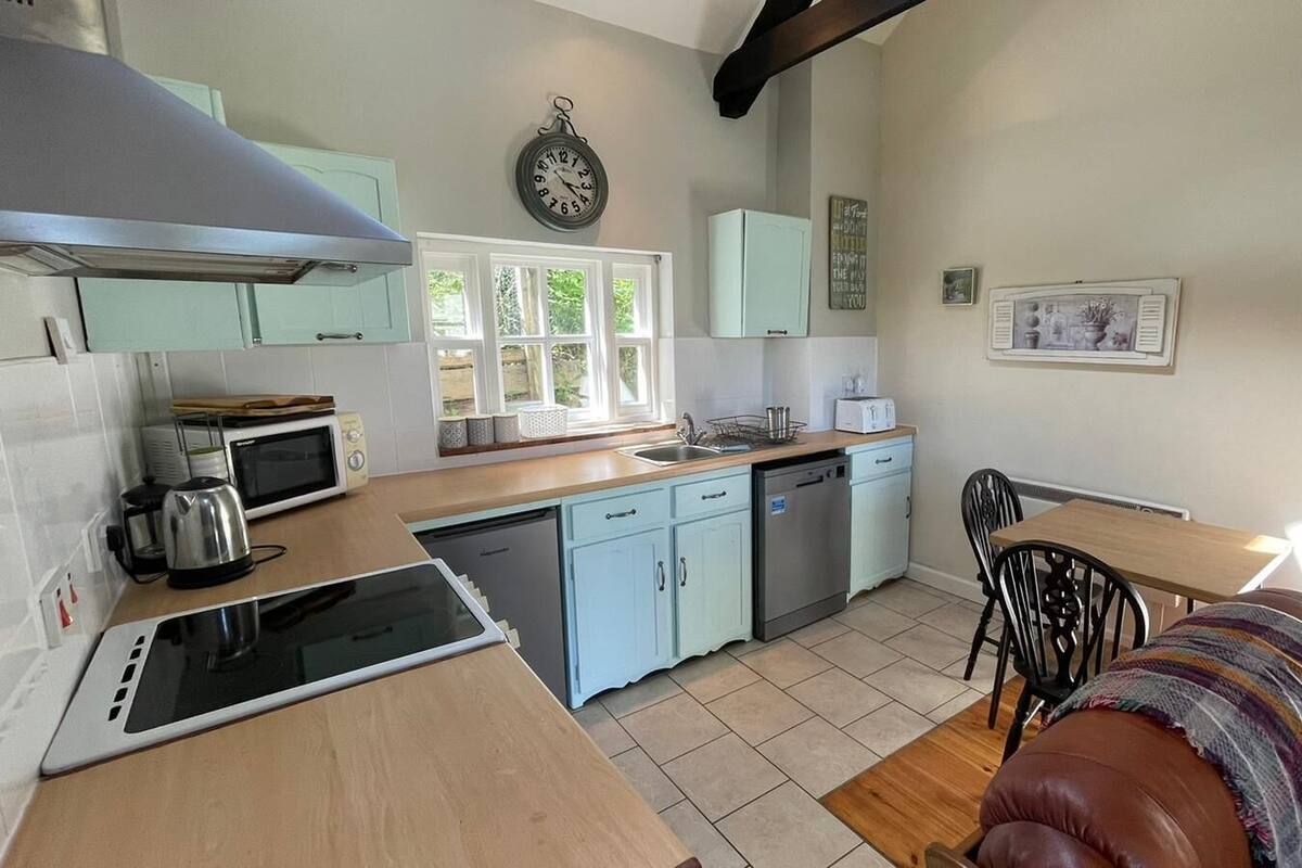 A compact kitchen with a microwave, toaster, and sink. There is a window providing natural light and a clock on the wall.
