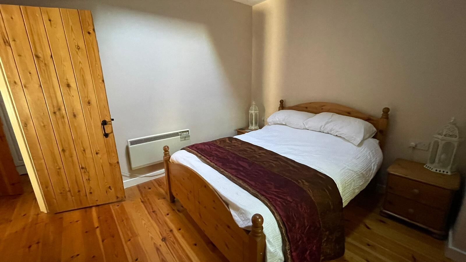 A bedroom with a wooden bed, a nightstand, a white radiator, and a wooden door.