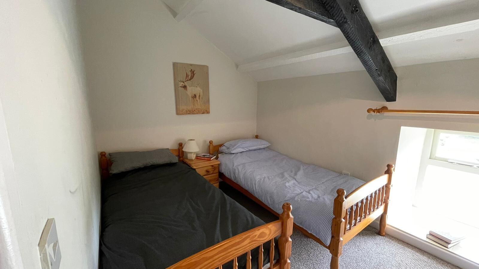 A small, single-room accommodation with two wooden beds, a nightstand, a lamp, and a painting of a deer on the wall.