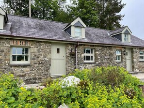 A stone house with a gabled roof, multiple windows, and a front door. - Crug Yr Eryr Isaf (Llandysul)