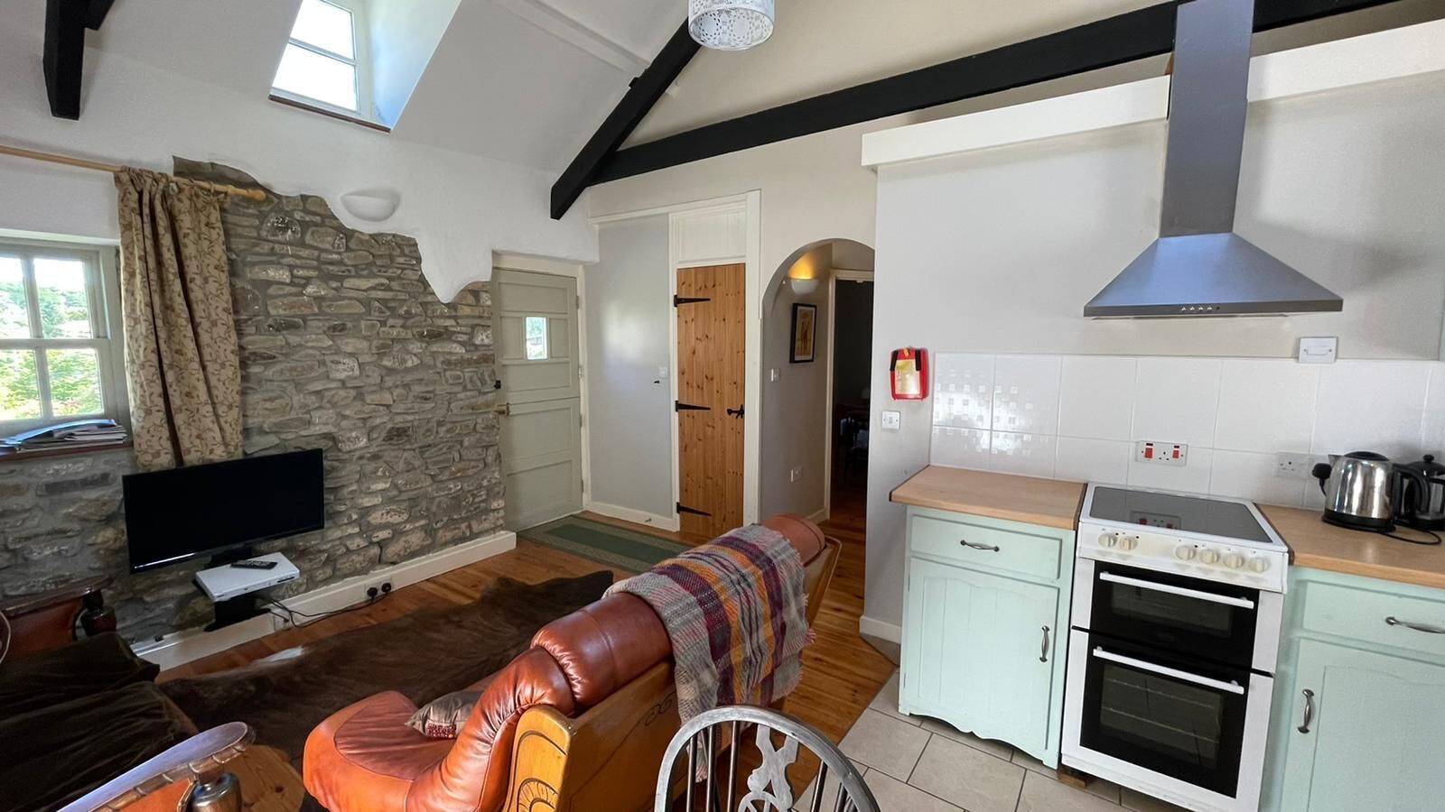 Una sala de estar acogedora con pared de piedra, televisor, sofá y una zona de cocina con estufa y armarios.