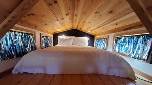 Une chambre à coucher avec un grand lit, des poutres apparentes en bois au plafond et des fenêtres avec des rideaux.