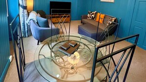 A living room with a glass coffee table, blue walls, a sofa, and a TV. - Old Spittal Hospital Apartment (Stirling)