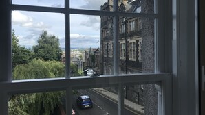 A view through a window of a street with a blue car driving on the road, buildings, and greenery. - Old Spittal Hospital Apartment (Stirling)
