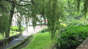 A pathway lined with lush greenery and a stone wall, leading to a grassy area with a view of a road and buildings in the distance. - Old Spittal Hospital Apartment (Stirling)