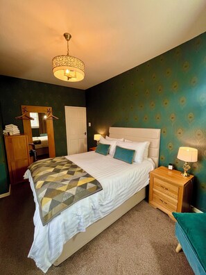 A bedroom with a bed, bedside table, lamp, dresser, mirror, and wardrobe. - Old Spittal Hospital Apartment (Stirling)