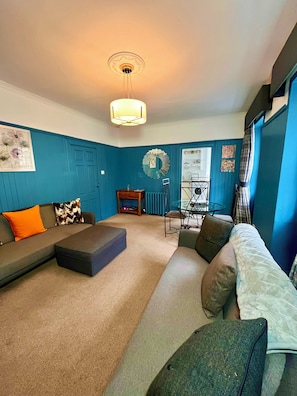 A living room with a sectional sofa, a coffee table, a dining table with chairs, a radiator, and a wall-mounted mirror. - Old Spittal Hospital Apartment (Stirling)