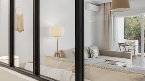 Ein modernes Wohnzimmer mit einer Couch, einer Lampe und einem Essbereich, der durch eine Glastür sichtbar ist.