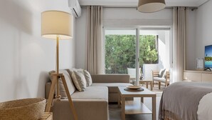 Ein modernes Hotelzimmer mit einer Couch, einem Bett, einem kleinen Tisch, einer Lampe und Blick ins Freie.