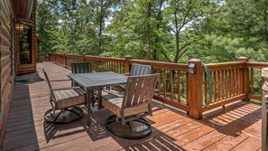 A wooden deck with a table and chairs, surrounded by a wooden railing and trees. - Tumnus Ridge - Super Dog Friendly | Hot tub | Fire Pit (Morganton)