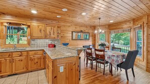 A wooden cabin interior with a kitchen, dining area, and large windows. - Tumnus Ridge - Super Dog Friendly | Hot tub | Fire Pit (Morganton)