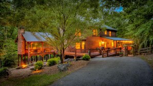 A log cabin with a porch and a covered walkway, surrounded by trees. - Tumnus Ridge - Super Dog Friendly | Hot tub | Fire Pit (Morganton)