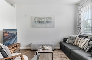 Un soggiorno moderno con un divano grigio, un tavolino in legno, una panca grigia e un quadro appeso al muro.