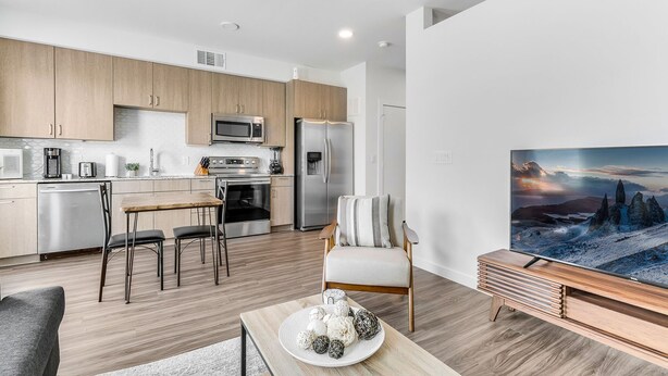 A modern kitchen with stainless steel appliances, a dining area with a wooden table and chairs, and a living room with a large flat-screen TV and a cozy armchair. - Downtown Modern Bungalow (Dallas)