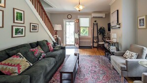 A living room with a dark green sofa, a grey armchair, a patterned rug, a wooden bench, and a staircase.