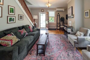 Un salon avec un canapé vert foncé, un fauteuil gris, un tapis à motifs, un banc en bois et un escalier.