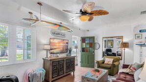 A living room with a ceiling fan, a television, a green door, and a view of the outdoors.
