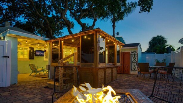 An outdoor patio area with a wooden gazebo, a fire pit, and outdoor seating.